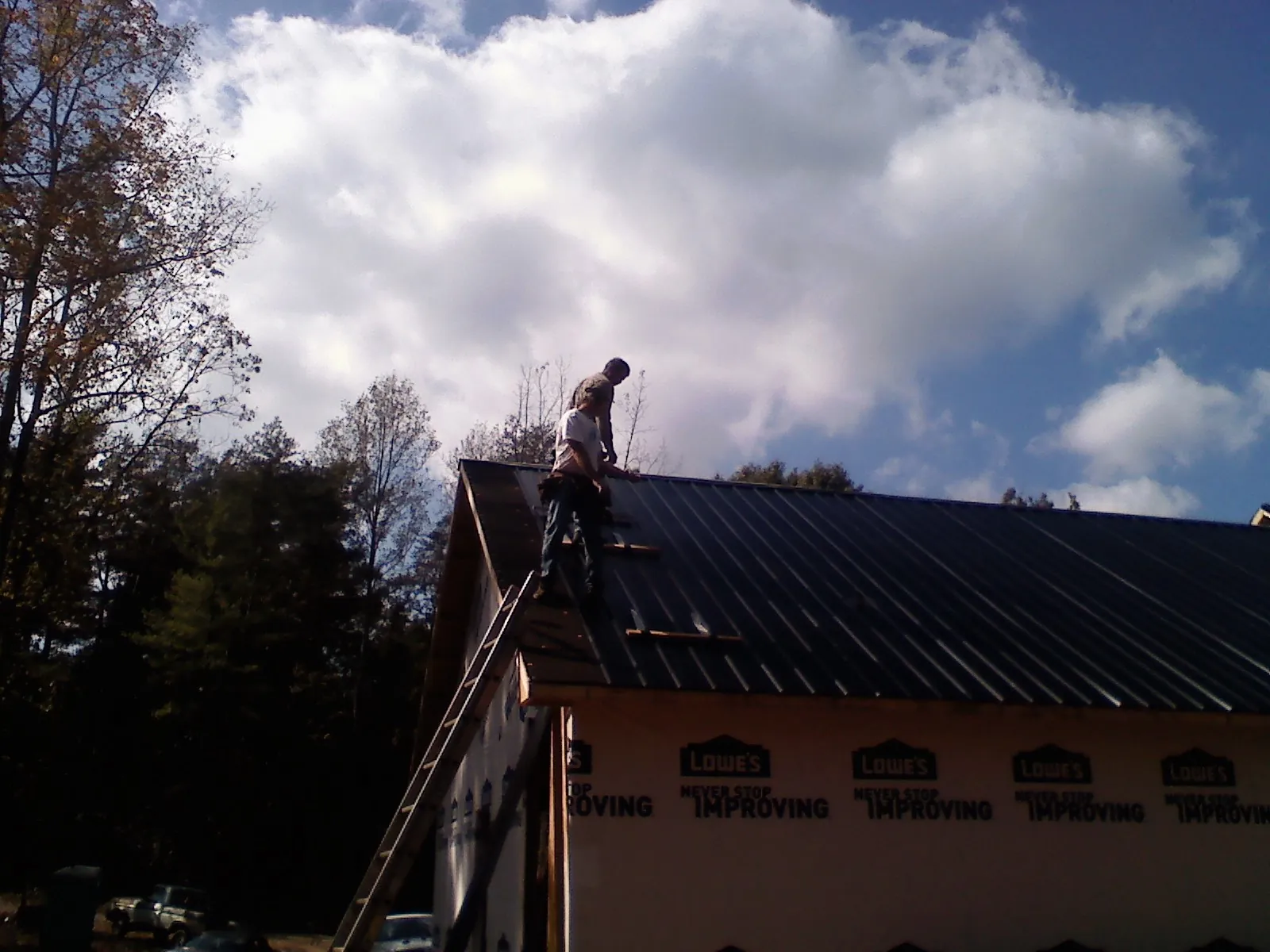 Roofer fastening dark metal panels high against a cloudy sky, from a Roof Inspection job in New Liberty
