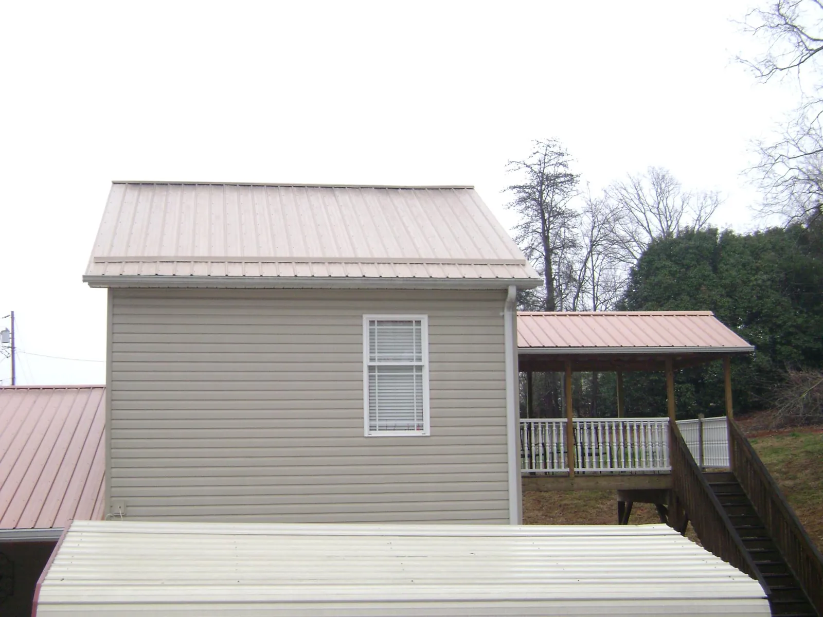 Tan metal roofs on a two story addition and attached porch, from a Roof Replacement job in New Liberty